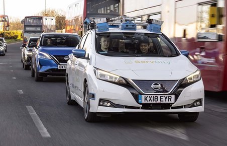 Selvkørende Nissan Leaf kører på vejen i Lodon omgivet af røde London-busser