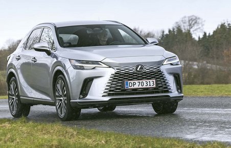 Sølvgrå Lexus RX plugin-hybrid kører på landevej med græs i forgrunden