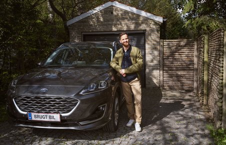 Mand står ved siden af sin brugte bil, som holder i en carport