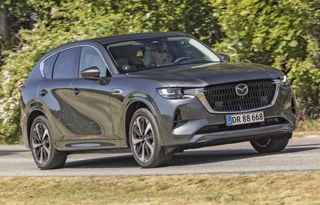 En Mazda CX-60 med stor dieselmotor kører på en landevej med træer i baggrunden