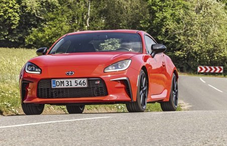 Rød Toyota GR86 kører på landevej med træer i baggrunden. 