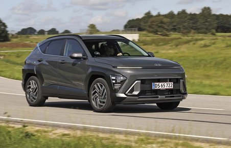 Hyundai Kona kører på landevej med græs i baggrunden.