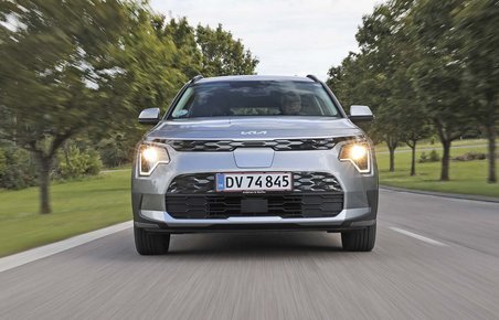 Elbilen Kia Niro EV set forfra, mens den kører på en allé.