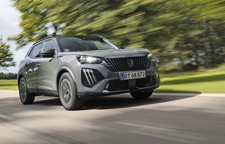 Elbilen Peugeot E-2008 set forfra, mens den kører hurtigt med træer i baggrunden.