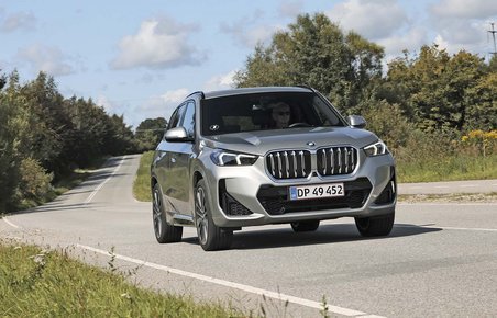 Elbilen BMW iX1 kører i et sving på en landevej med træer i baggrunden.