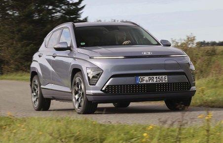 Elbilen Hyundai Kona kører på en landevej med græs foran og bagved.