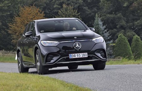 Elbilen Mercedes EQE SUV kører på en landevej med træer i baggrunden.