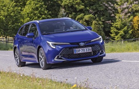 Hybridbilen Toyota Corolla Touring Sports kører på en landevej med træer i baggrunden