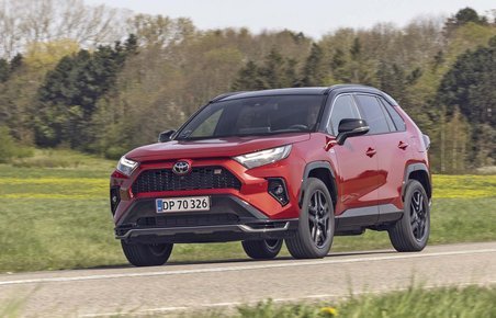 En rød Toyota RAV4 kører på en landevej med træer i baggrunden
