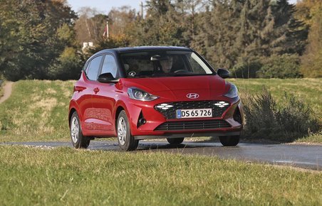 En rød Hyundai i10 kører på en landevej med træer i baggrunden