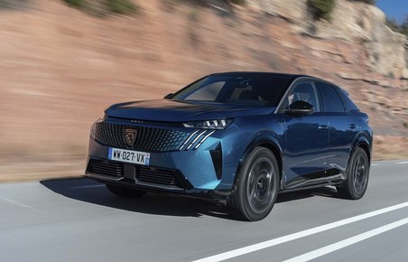 En Peugeot E-3008 elbil set forfra, mens den kører på en bjergvej med klipper i baggrunden