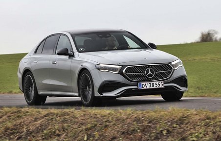 En sølvgrå Mercedes E-klasse set forfra, mens den kører på en vej med græs i baggrunden