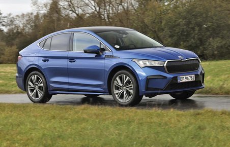 En blå Skoda Enyaq Coupé set fra siden, mens den kører på en landevej med græs i forgrunden