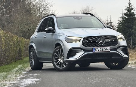 En sølvgrå Mercedes-Benz GLE holder på en vej med en hæk i baggrunden.