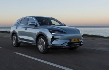 En sølvgrå BYD Seal U kører langs havet ved solnedgang.