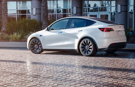 Hvid Tesla Model Y holder foran bygning og palmetræer. 