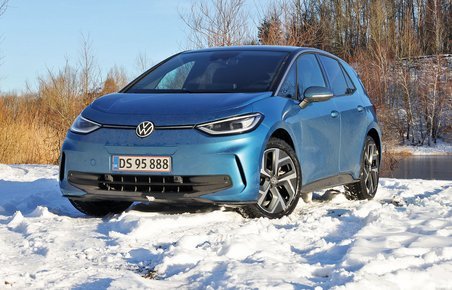 En blå VW ID.3 holder i sne med en skovsø i baggrunden