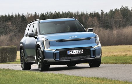 En blå Kia EV9 kører på en landevej med græs i baggrudnen