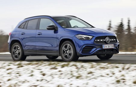 En blå Mercedes-Benz GLA 250 e kører på en landevej med sne i forgrunden og træer i baggrunden