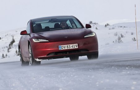 En rød Tesla Model 3 set forfra kører i snelandskab