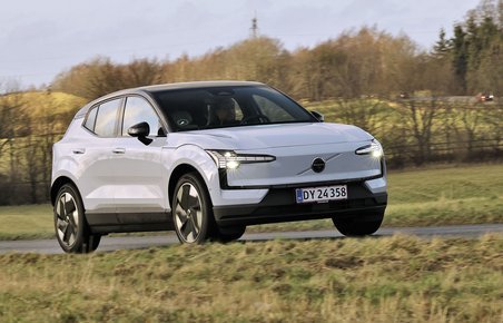 En hvid Volvo EX30 kører på en landevej med græs på begge sider