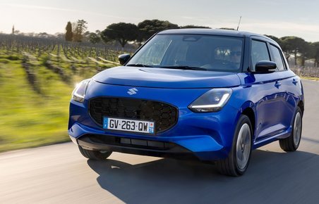 Blå Suzuki Swift kører på en vej med vinmarker i baggrunden