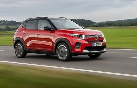 En rød Citroën ë-C3 kører på en vej med græs i baggrunden