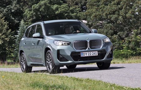BMW iX1 kører på en vej med træer i baggrunden