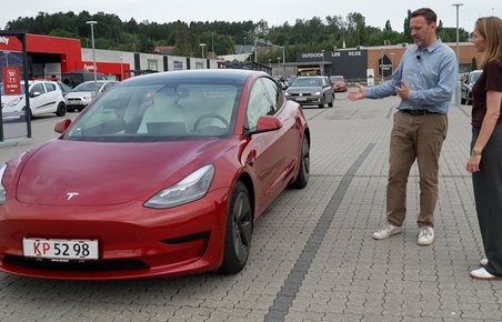 En mand og en dame kigger på en Rød Tesla Model 3