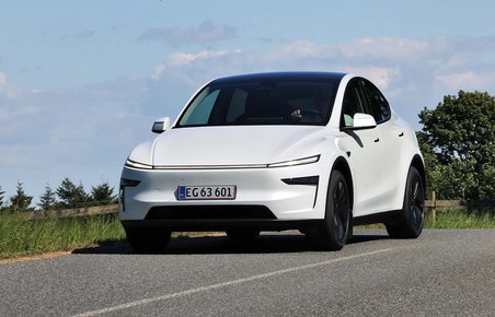 Tesla Model Y kører på en landevej med blå himmel i baggrunden