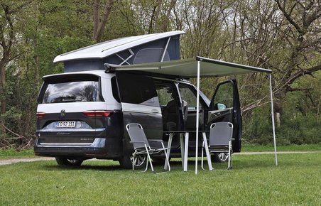 VW California med opslået tag og udslået markise holder på græsplæne